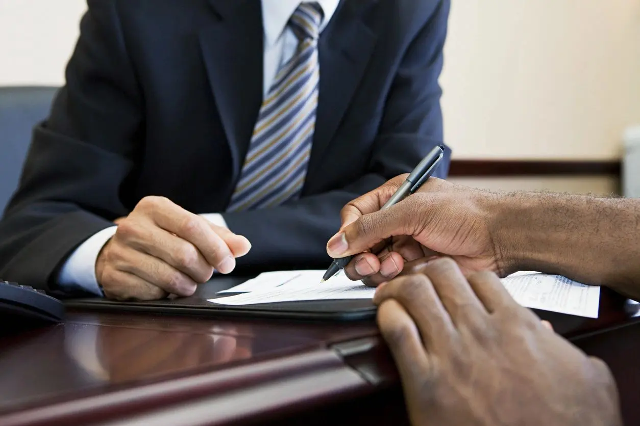 Two men sign a document at a desk.