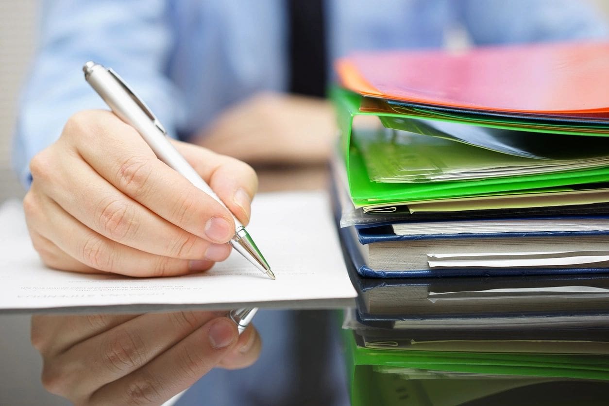 Hand signing document with pen and folders.