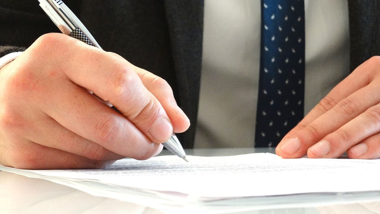 A hand signing a document with a pen.