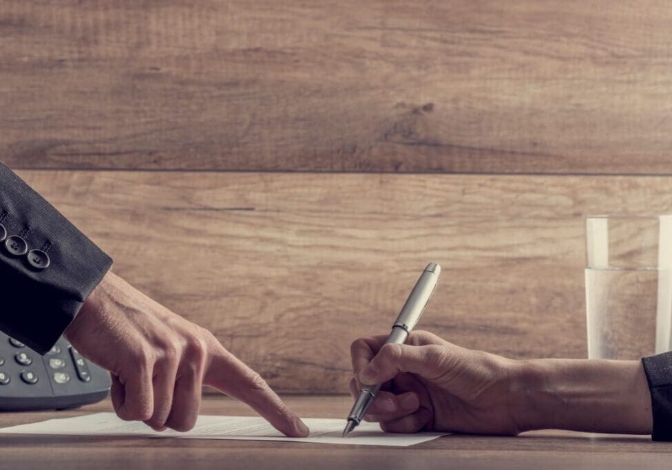 Person signing document with pen and finger.