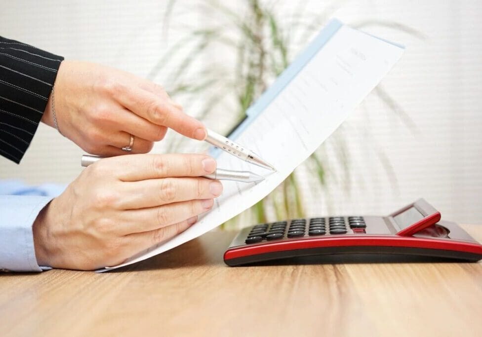 Person reviewing document with pen and calculator.